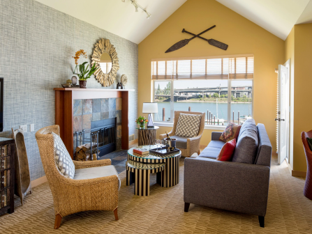 A cozy living room with a stone fireplace, patterned seating, a round table, and large windows showing a river view.