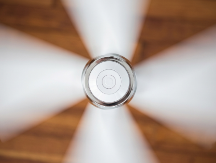 A close-up of a white three-blade ceiling fan centered on its hub, spinning above a wooden floor.