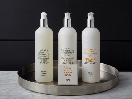 Three pump bottles for shampoo/body wash sit on a round tray, with a bar soap box in front against a dark wall.