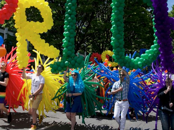 A colorful outdoor parade with spectators and performers holding balloon sculptures shaped like giant letters.