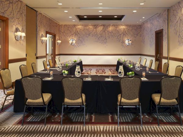 A set banquet table with place settings, chairs, flowers, and glass carafes in a formal meeting room, lit by ceiling lights.
