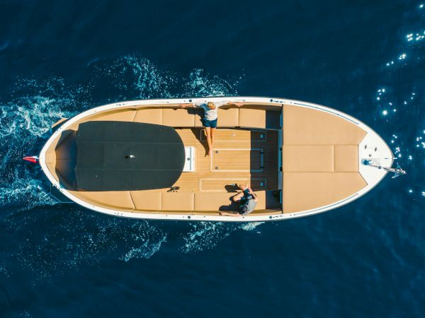 Aerial view of a luxury yacht speeding through blue ocean as people relax on deck and a wake trails behind.